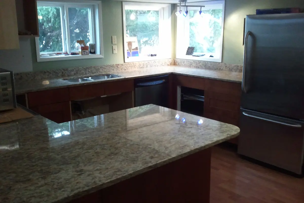 A granite countertop on stained wood base cabinets with a stainless sink, in a kitchen that is mid installation with some cabinet doors not yet fitted