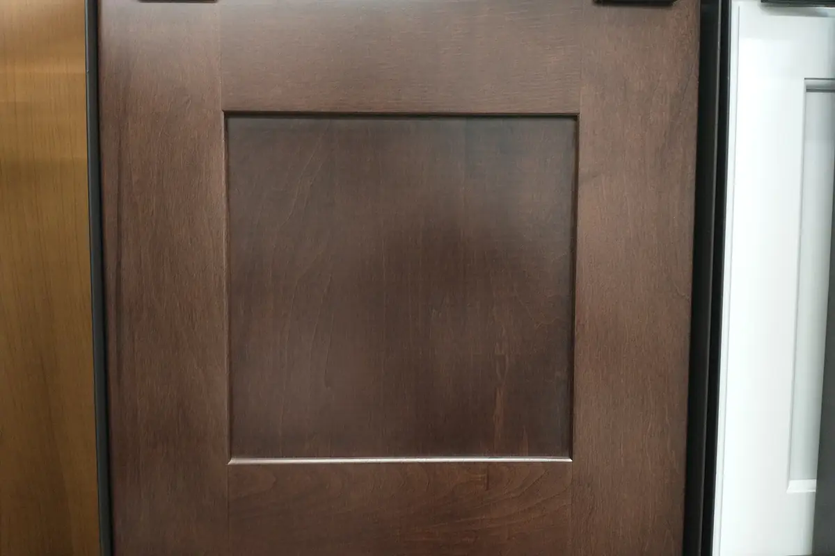 A dark stained shaker cabinet door with a wide frame, shown on a display rack beside other door samples, of the kind used for cabinet refacing in Riverside CA