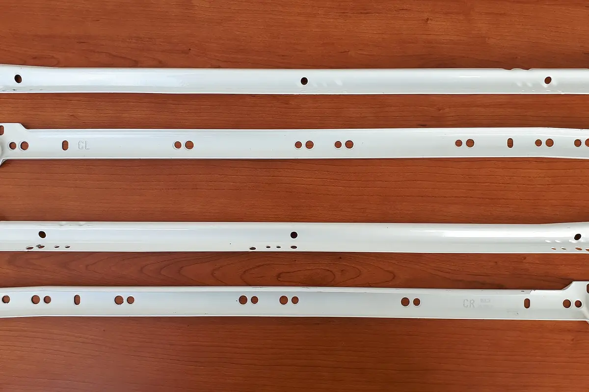 Four white epoxy coated bottom mount drawer slide rails laid out on a timber surface, showing the mounting hole pattern