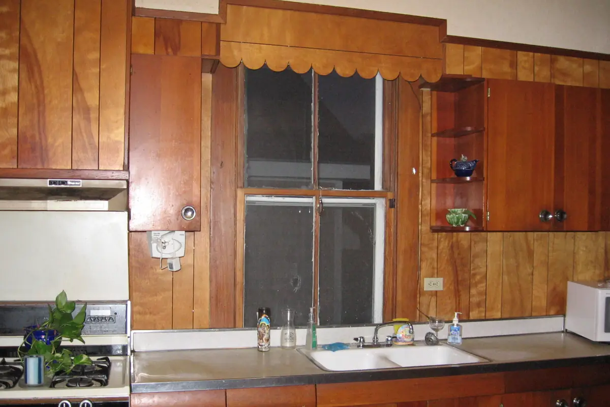 Original stained wood kitchen cabinets and a wood panelled wall in an older American house, typical of pre-1978 housing stock in Riverside CA