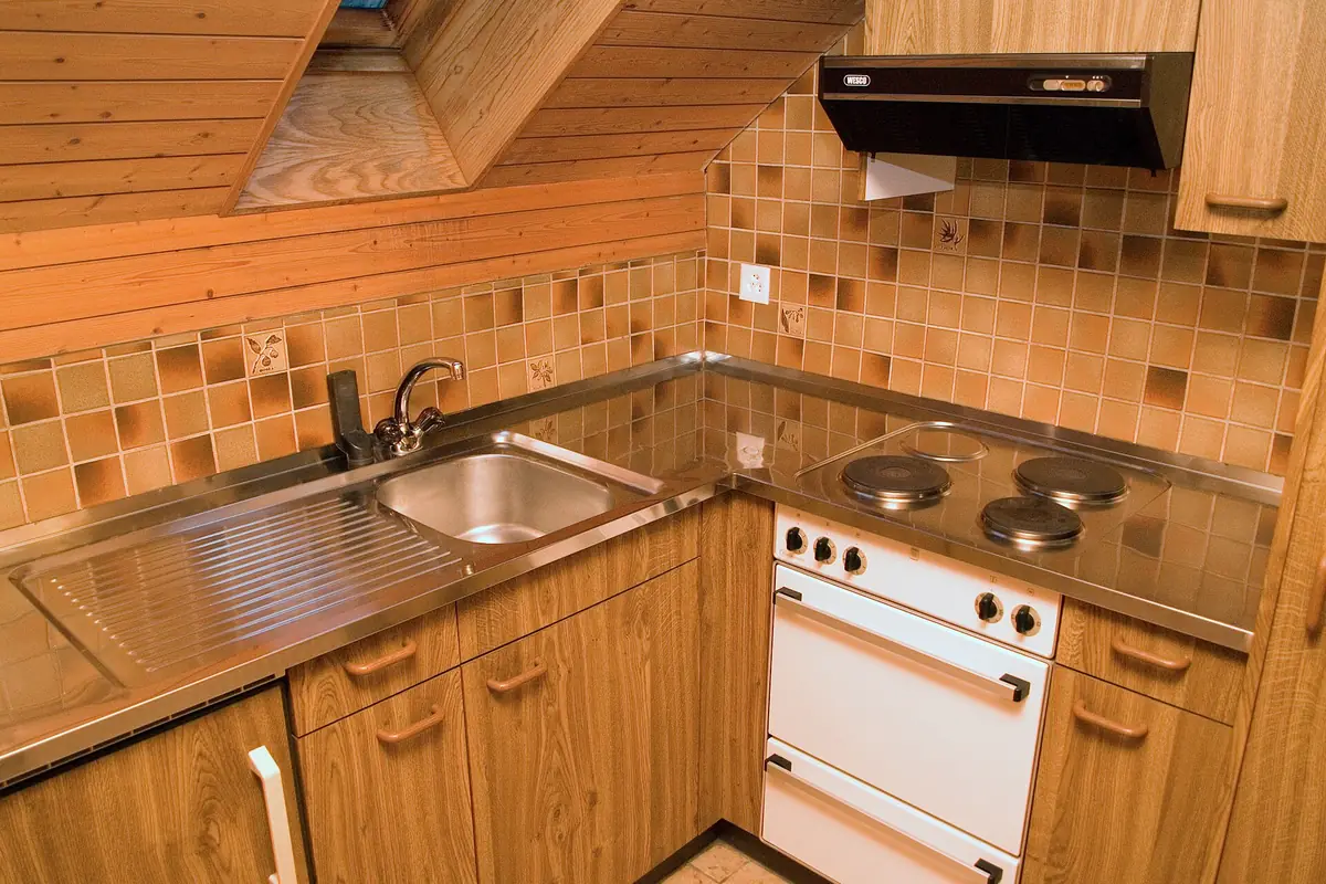 A compact wood fronted kitchen built into a sloping ceiling space with open shelving above the counter