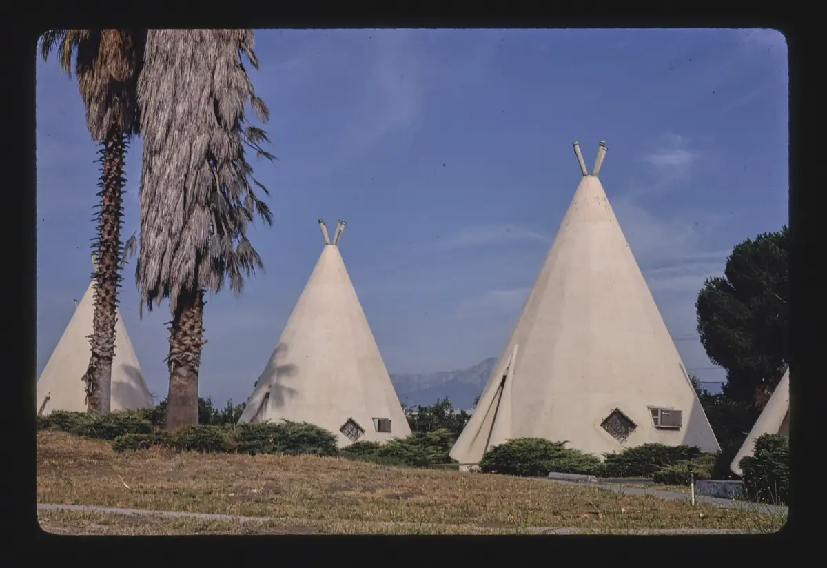 The Wigwam Motel on Route 66 in Rialto California, a row of white conical cabins among planting and palm trees