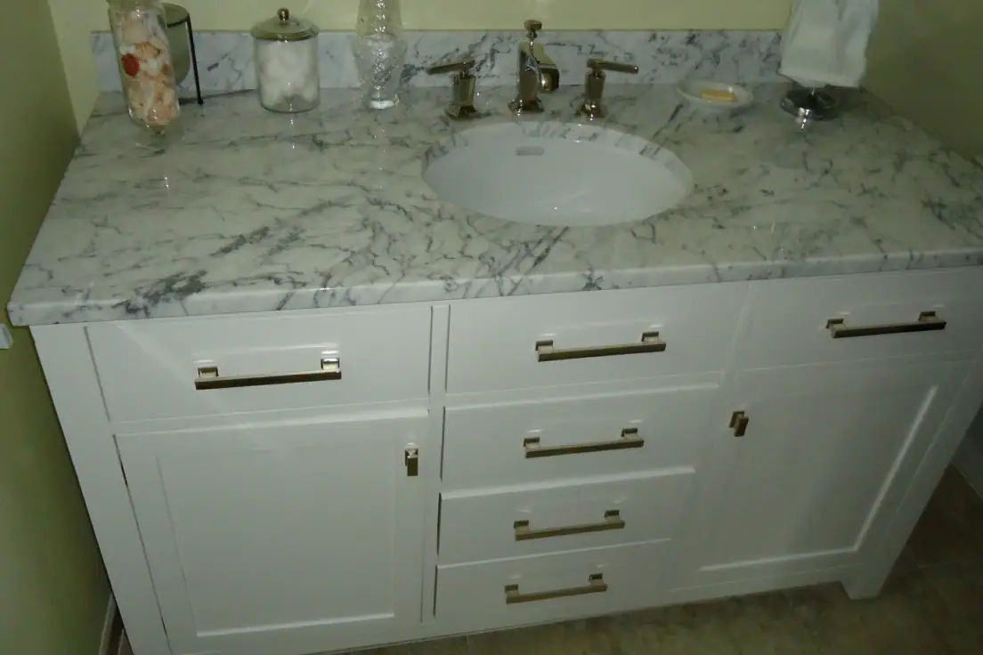 A white painted shaker style bathroom vanity with a marble top, undermount basin and a bank of three drawers, in a residential bathroom